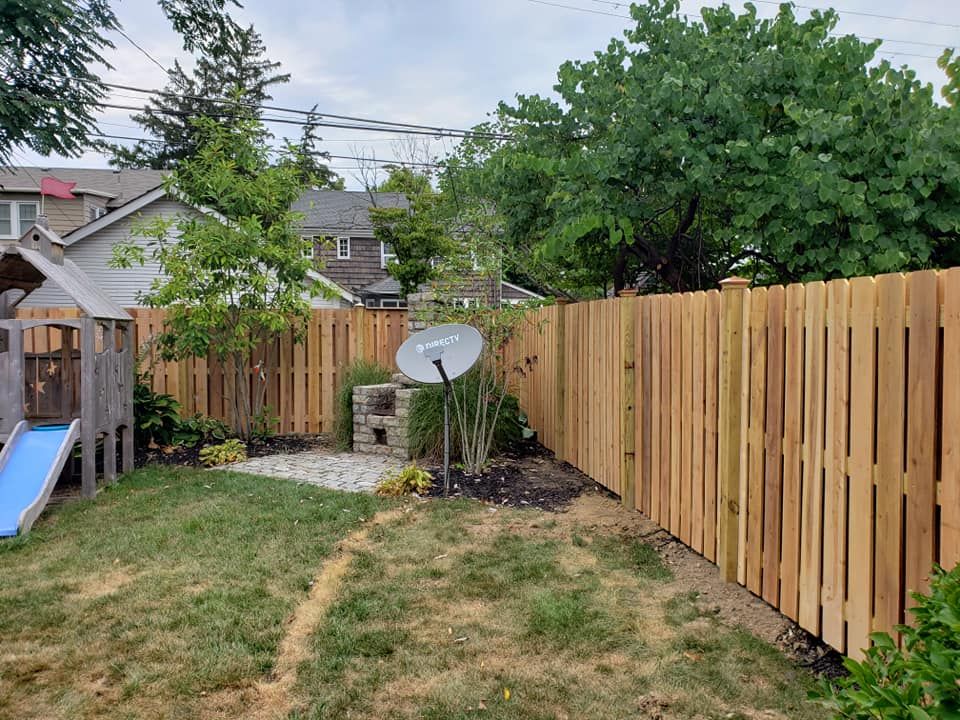 A wooden fence surrounds a backyard with a slide and a satellite dish.