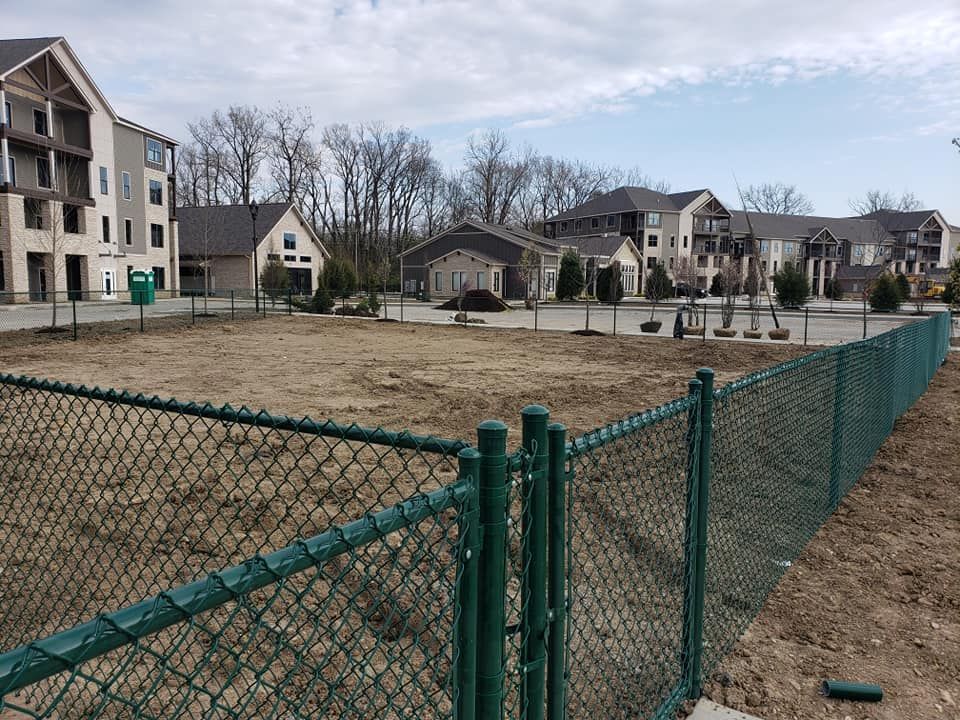 A chain link fence surrounds a dirt field in front of a building.