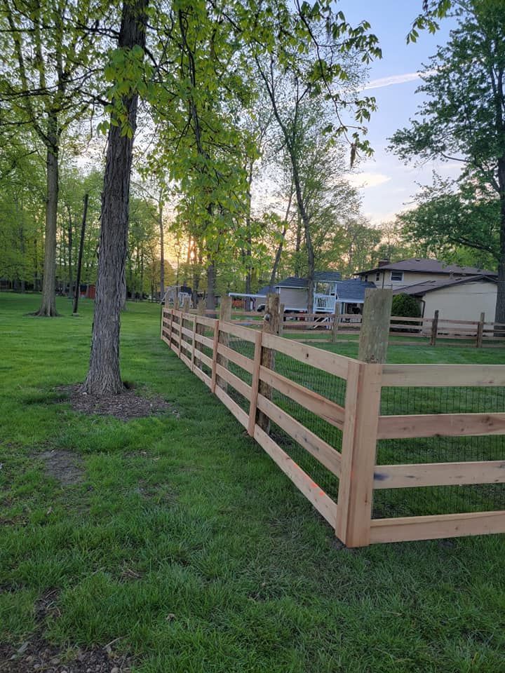 A wooden fence is in the middle of a lush green field.