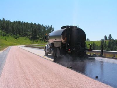 A truck is spraying asphalt on the side of a road.