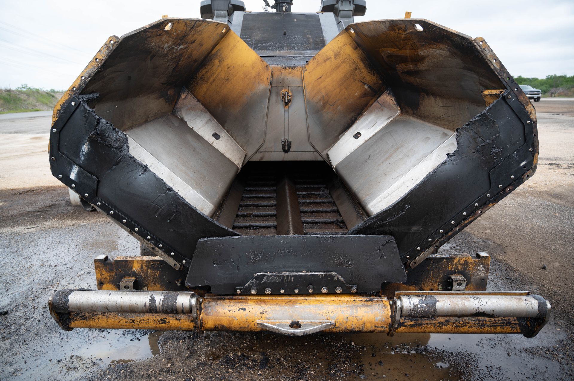 A yellow and black asphalt paving machine is parked on the side of the road.