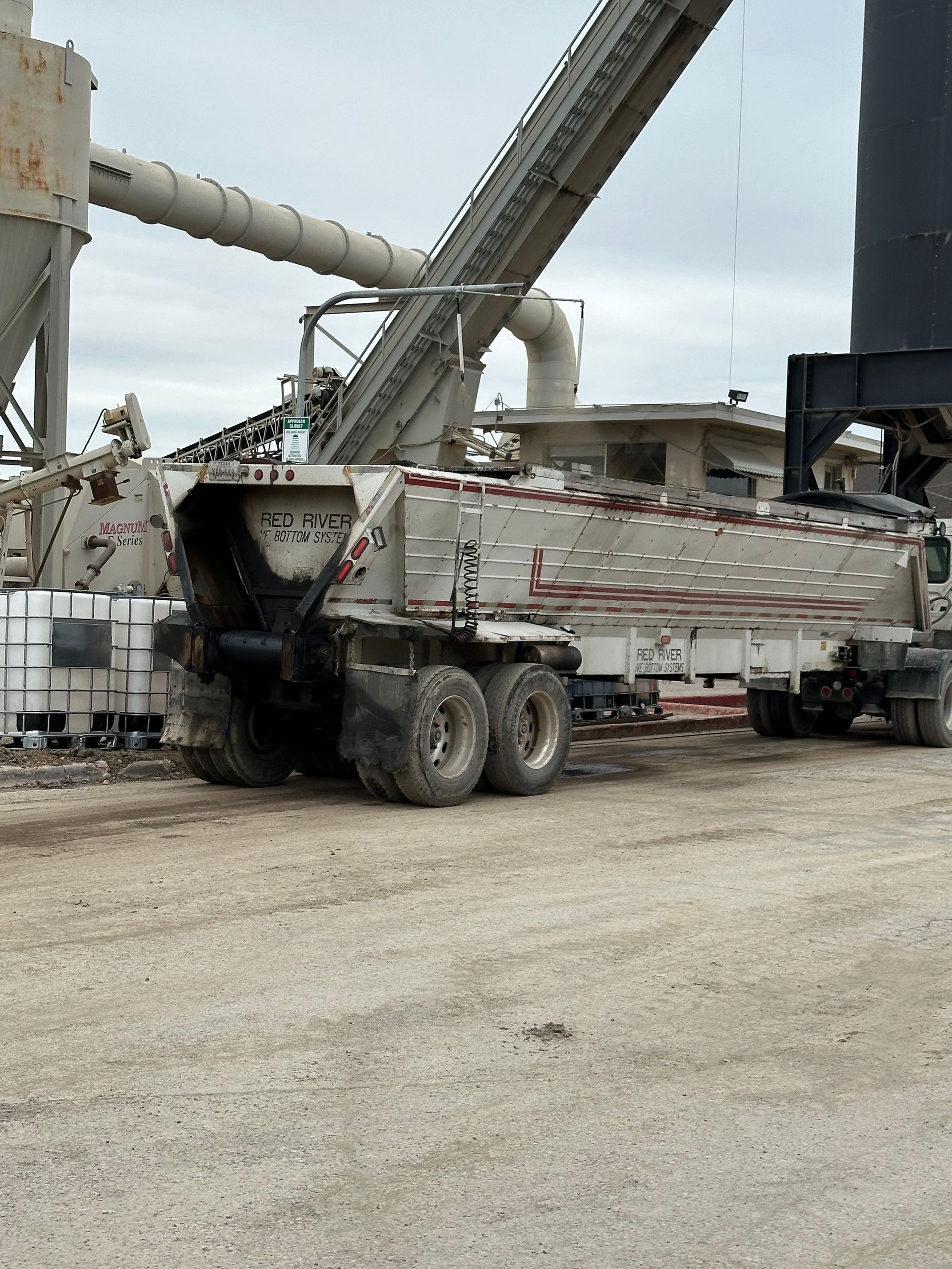 A dump truck is parked in a dirt lot in front of a factory.