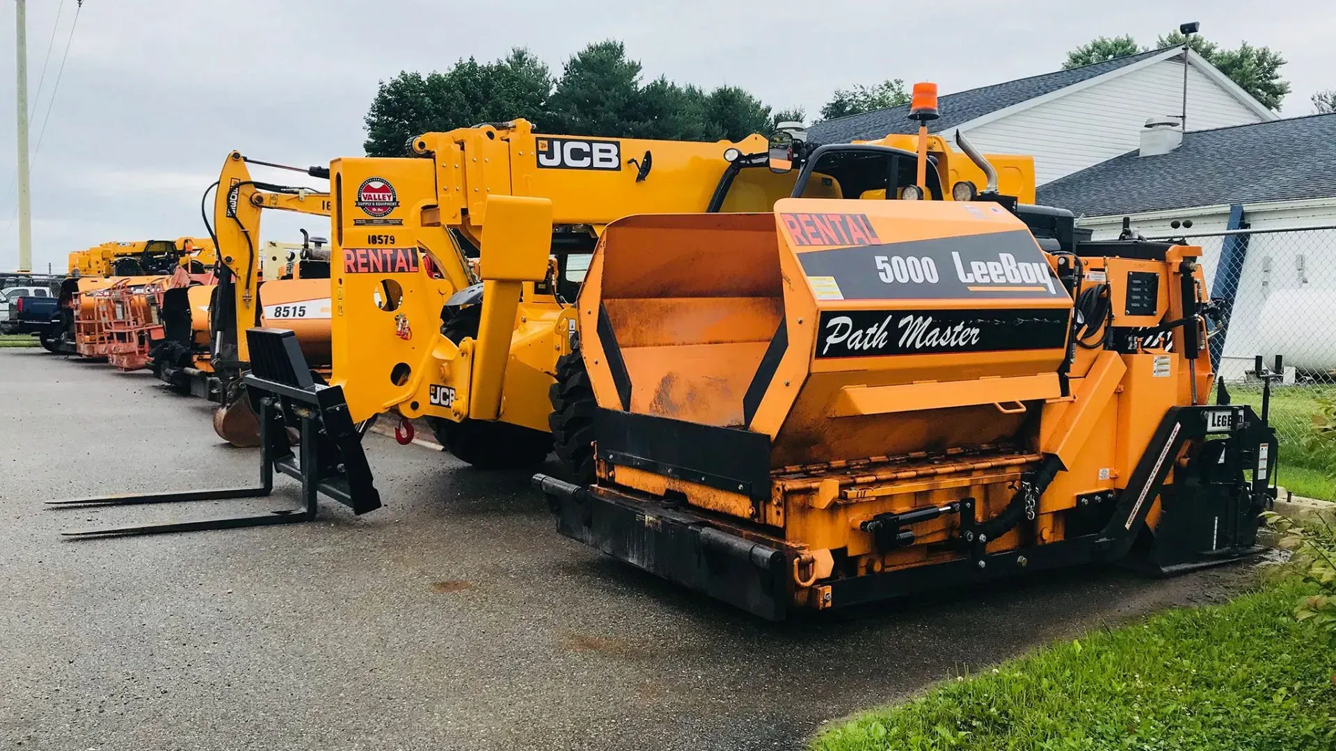 A row of jcb asphalt pavers are parked on the side of the road