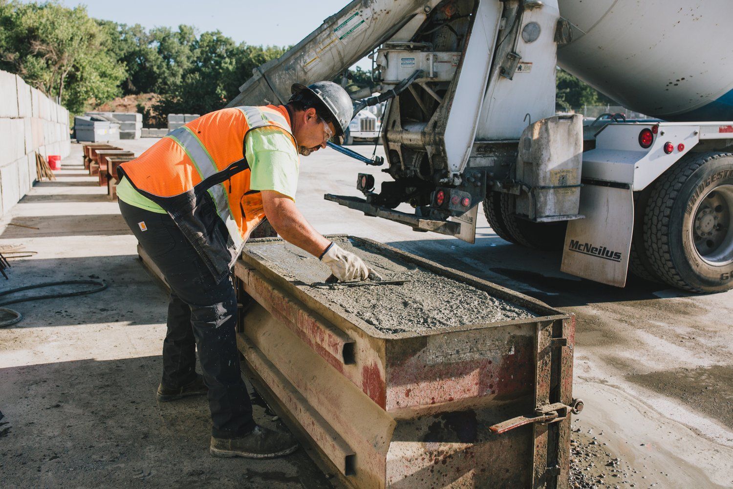 A construction worker is pouring concrete into a container.