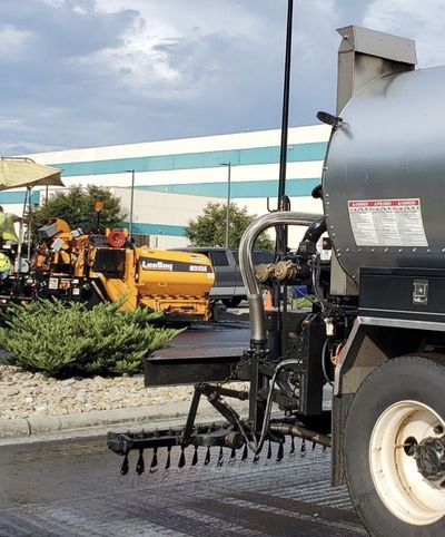 A truck is spraying asphalt on a street in front of a building.