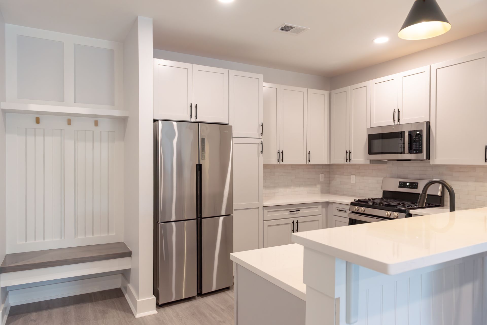 White kitchen with stainless steel appliances, a breakfast bar, and a bench by a coat rack.