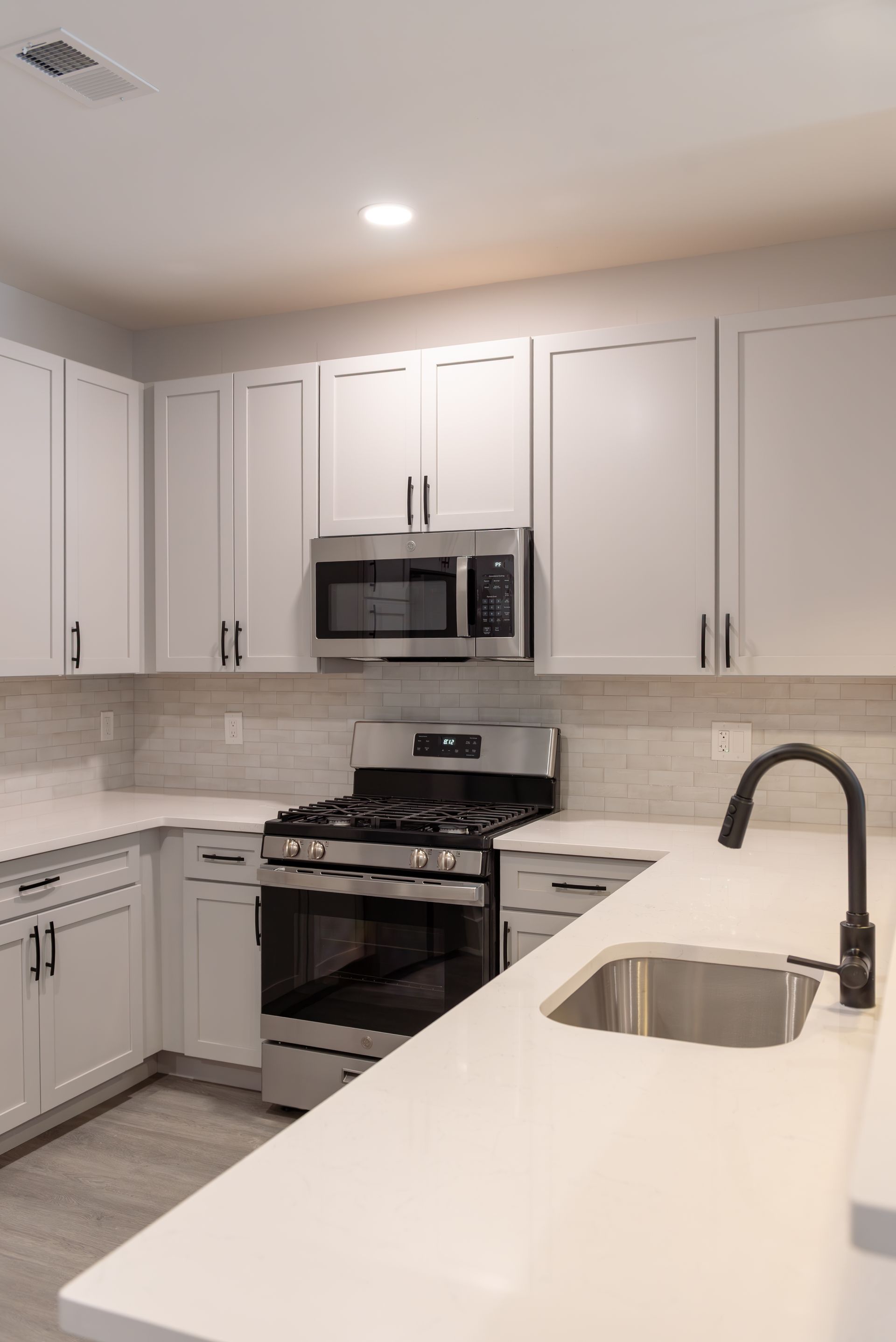 White kitchen with cabinets, gas stove, microwave, and a sink with a black faucet.