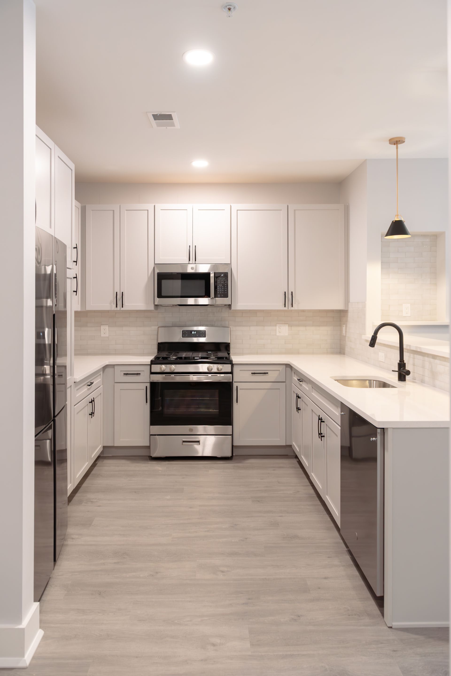 Modern white kitchen with stainless steel appliances, light wood floor.