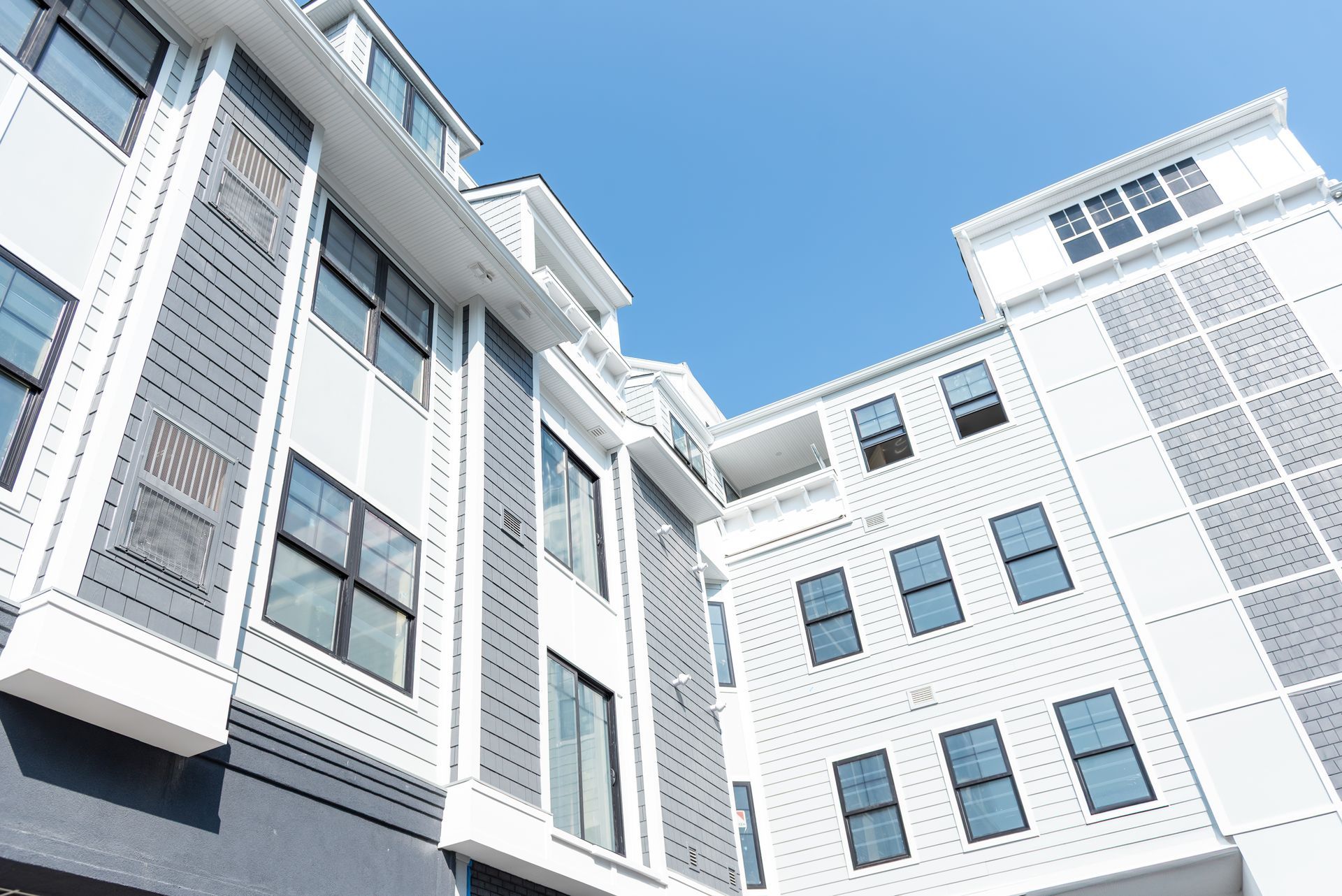 Multi-story building with white and gray siding against a bright blue sky.