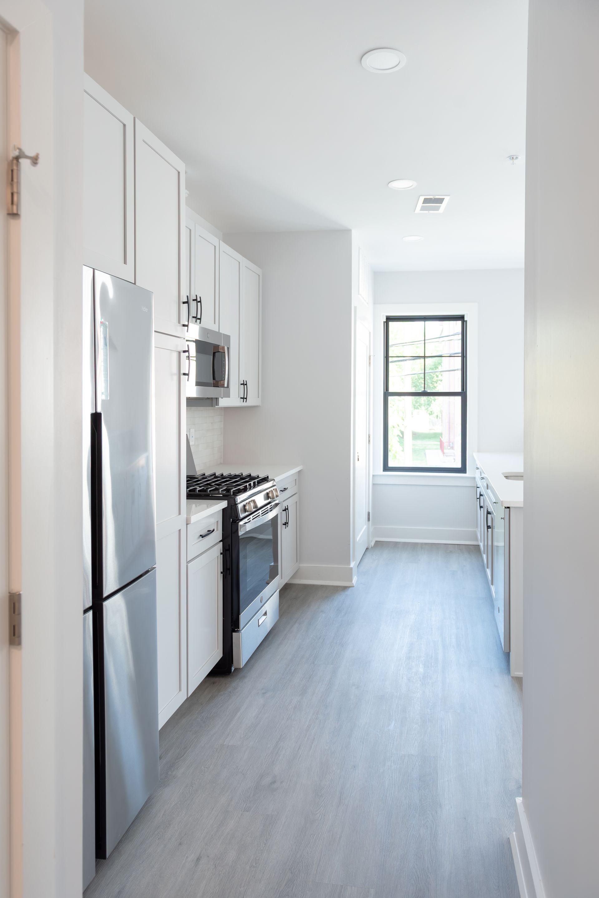 White kitchen with stainless steel appliances, gray floor, and a window.
