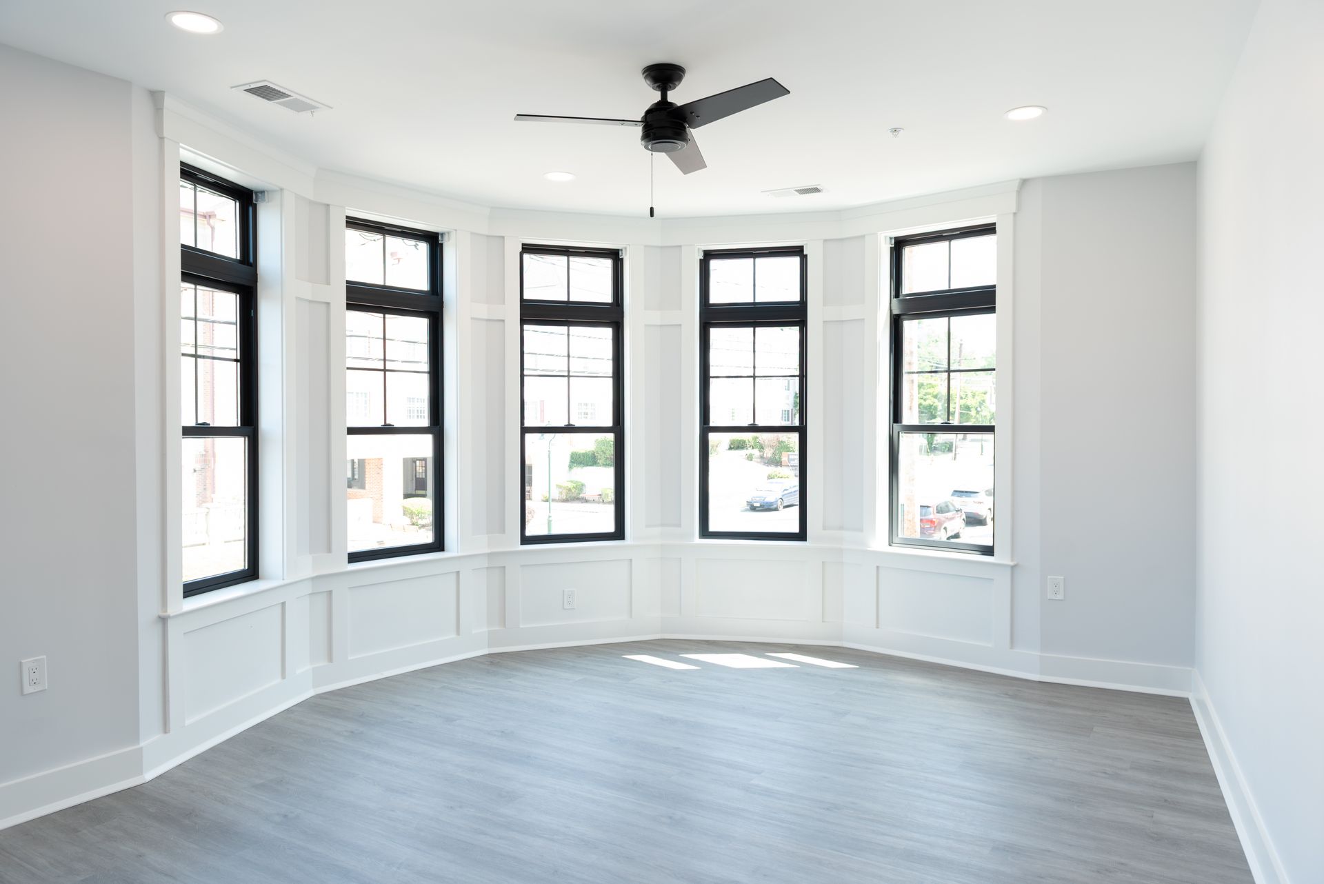 Empty room with curved bay windows, black frames, and gray floors. Black ceiling fan.