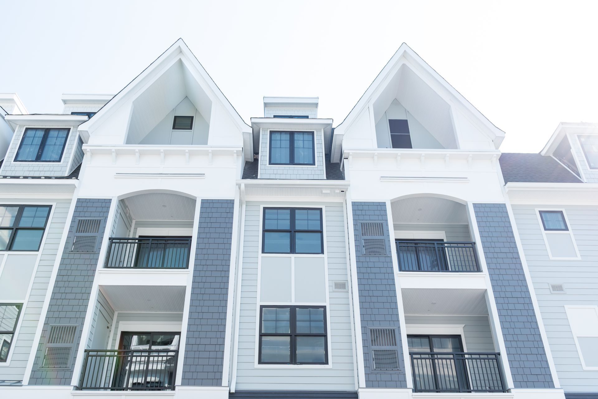Multi-story apartment building with gray and white facade, balconies, and black-framed windows.