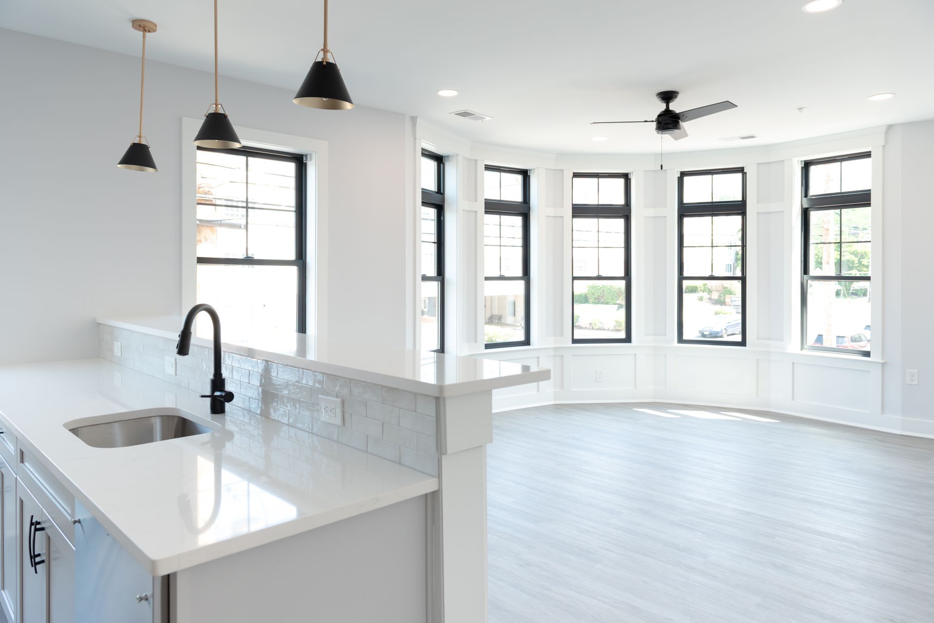 Bright, white kitchen and living space with a large curved window wall and overhead lighting.