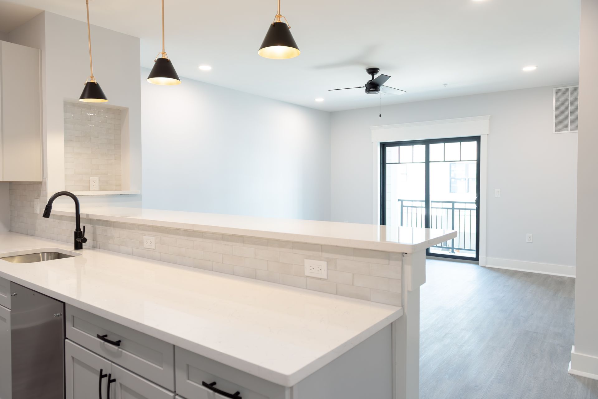 Modern kitchen with white countertops and cabinets, breakfast bar, and sliding glass door to a balcony.