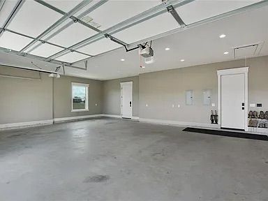 Empty, gray garage with white door, ceiling, and trim. Concrete floor, overhead door opener.