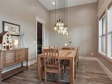Dining room with wooden table, chairs, and rustic decor, lit by hanging lightbulbs.