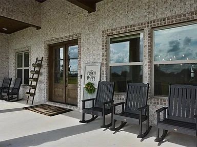 A porch with rocking chairs, brick walls, and wooden door and windows.