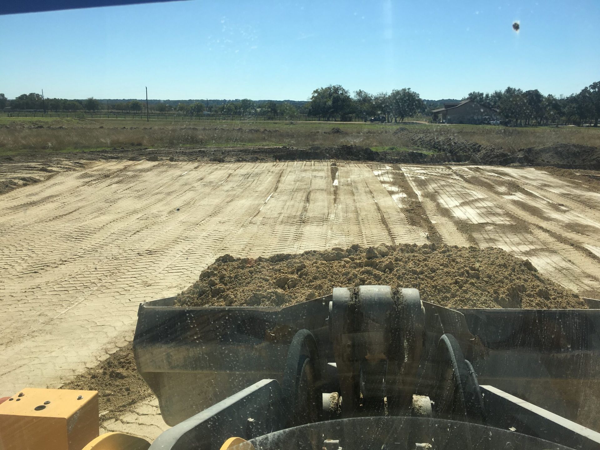 Front-view of a loader scooping dirt, leveling a sandy construction site under a blue sky.