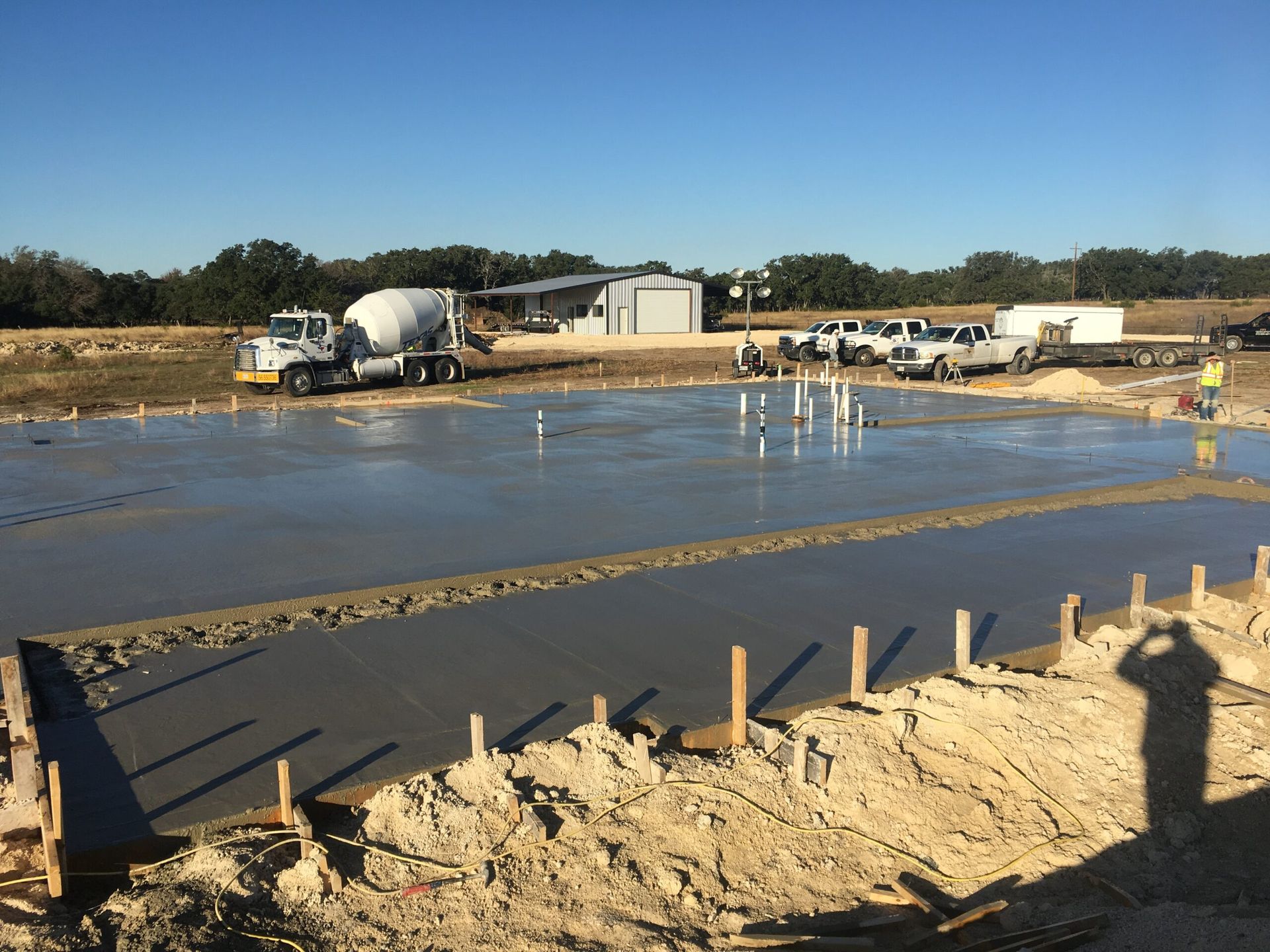 Fresh concrete foundation with a truck, pipes, and a shed under a blue sky. Construction site.
