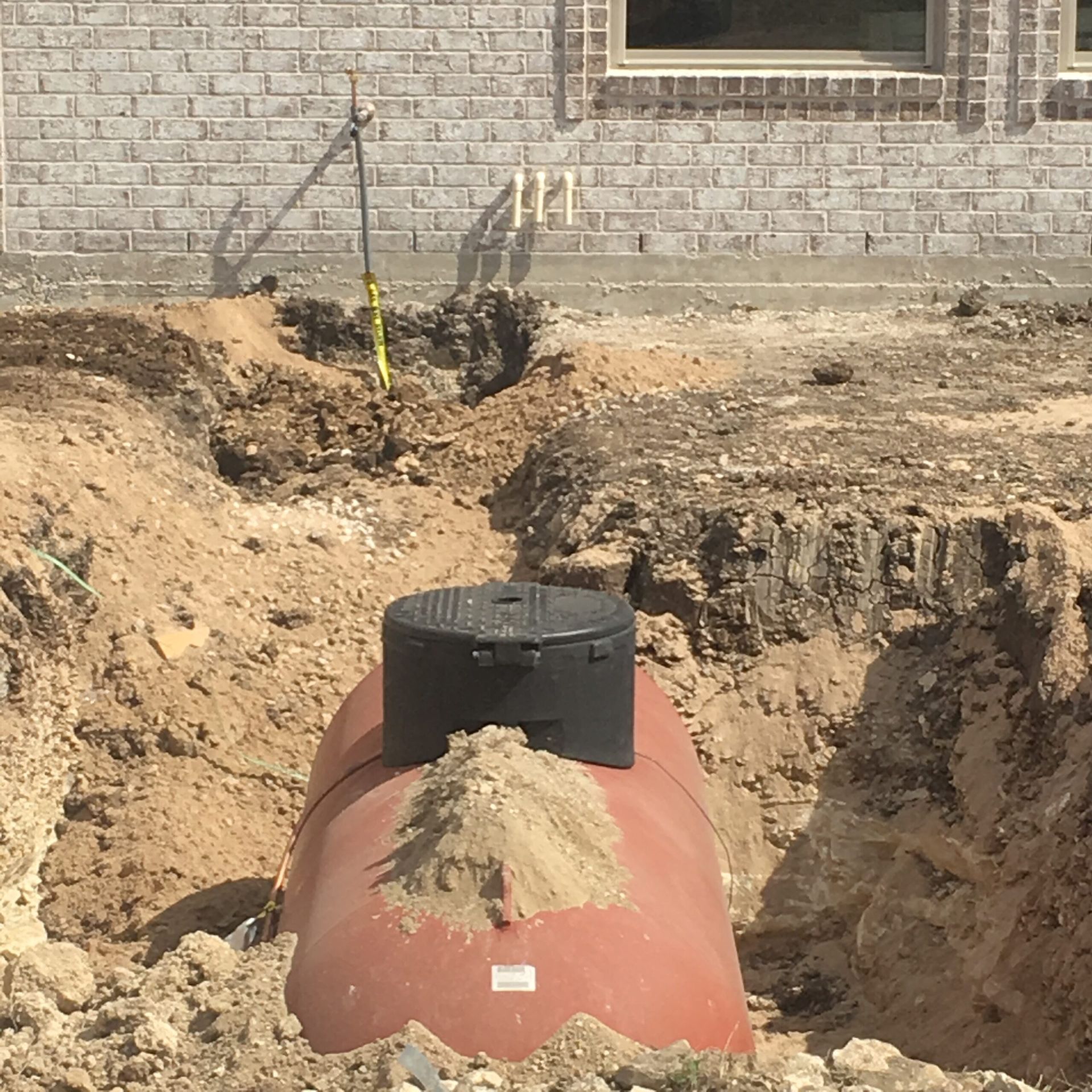 Brown septic tank in a dirt trench near a brick wall.