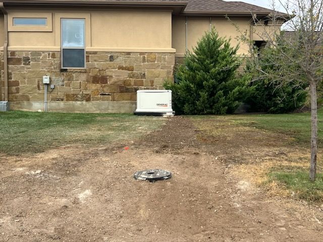 Backyard with generator, dirt patch leading to a septic tank cover, and a house with stone facade.