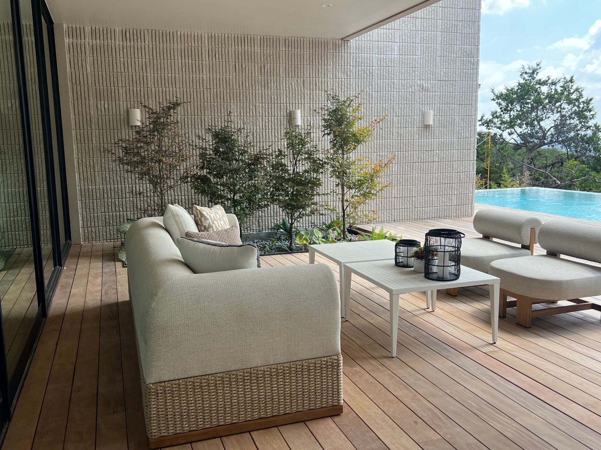 Outdoor patio with a couch, small trees, and a pool in the background.