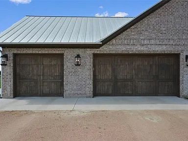Two-car garage with dark wood doors and brick exterior. Metal roof under a blue sky.