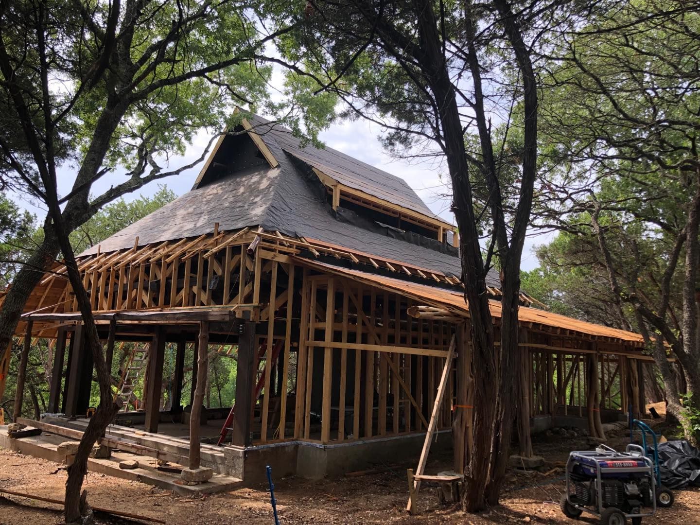 A wooden house under construction in a wooded area. The roof is partially completed.