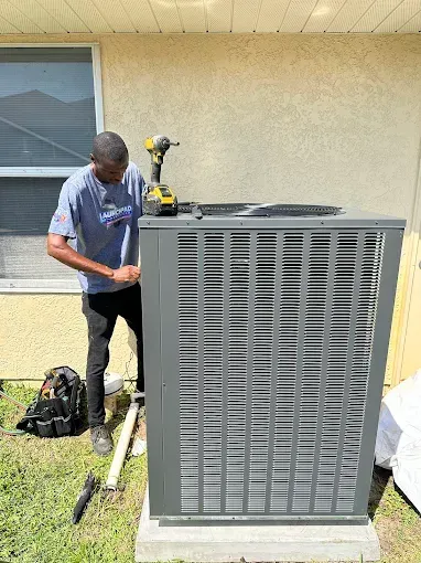 Technician working beside a large gray HVAC unit outdoors with tools and equipment on the grass