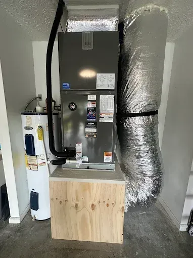 Furnace and HVAC unit in a utility closet with ducts, pipes, and a wooden platform.