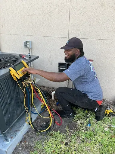 Technician kneeling beside HVAC unit, using a yellow tool on tangled wires outdoors.
