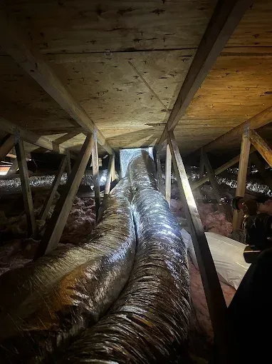 Attic crawlspace with large silver insulated ducting under wooden beams and floorboards