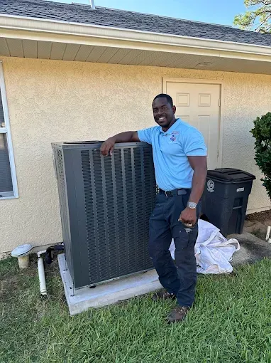 Man standing beside an outdoor HVAC unit near a house, with a lawn and trash bins nearby.