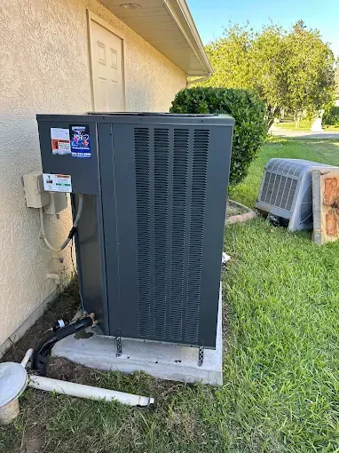 Outdoor HVAC unit beside a house, with a small fenced enclosure and grass yard nearby