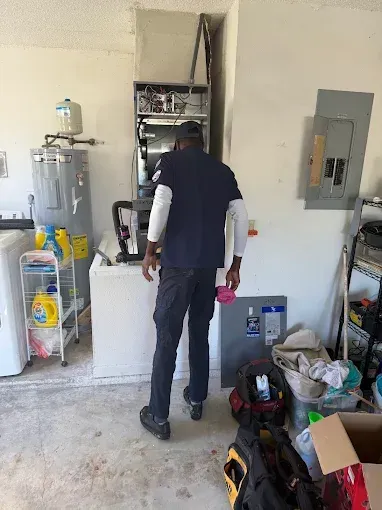 Person standing in a cluttered utility room facing an open wall cabinet