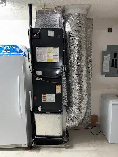 Indoor HVAC unit with ductwork beside a white appliance in a utility room