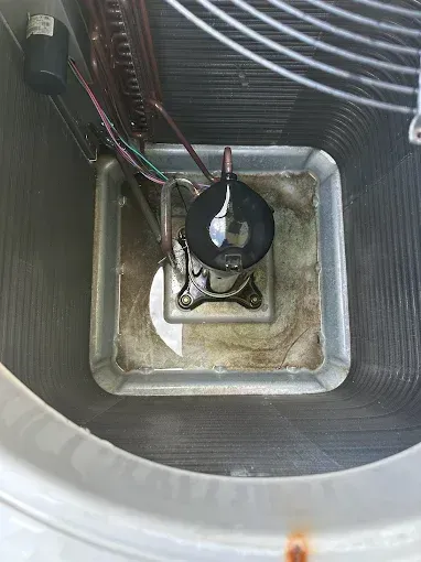 Black compressor mounted in a square metal housing with wires in a ribbed cylindrical enclosure