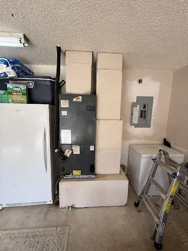 Garage/laundry area with stacked moving boxes around a refrigerator, storage items, and a step ladder