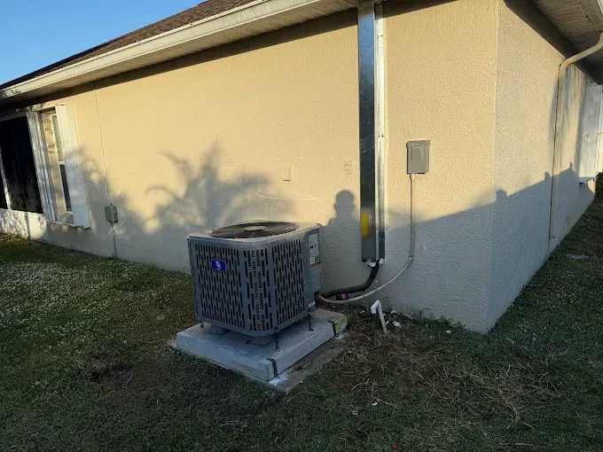Outdoor air conditioner unit beside a beige house with utility meter and conduit on the wall