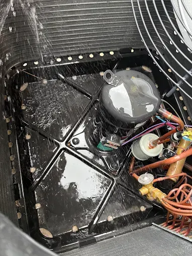 Inside an HVAC unit, showing wiring, a compressor, and dusty black interior panels.