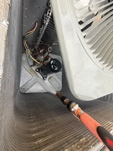 Close-up of HVAC fan compartment with exposed wiring and orange vacuum hose connected during maintenance