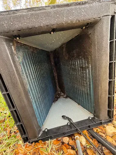 Open outdoor HVAC duct with blue metal interior and debris at the bottom