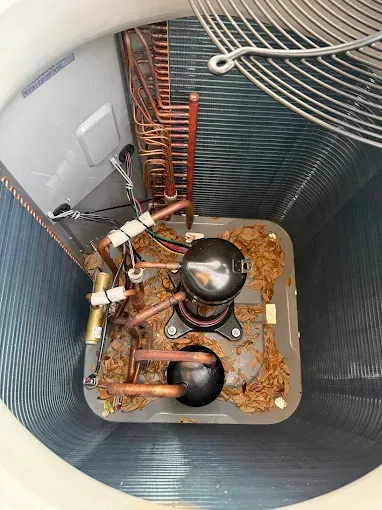 Top-down view of a furnace interior with two rusted black components and copper tubing inside a metal chamber