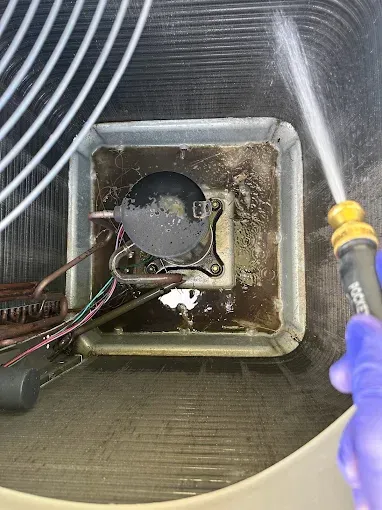 Gloved hand using a hose to clean a dirty square drain or sump in a sink basin