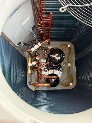 Inside a white bucket, copper pipes and black compressor components of a refrigeration unit are visible.