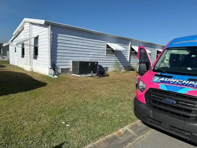 White house exterior with pink-and-blue van parked in driveway, front door open.