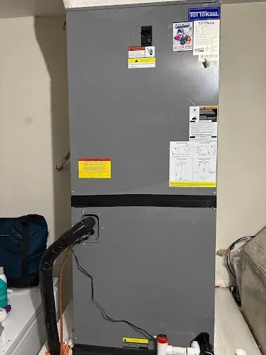Gray utility cabinet with labels and notes in a laundry or storage area, cords hanging from the left side.