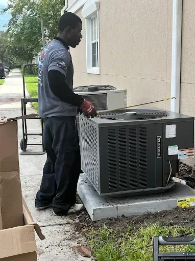 Technician servicing an outdoor HVAC unit beside a building wall