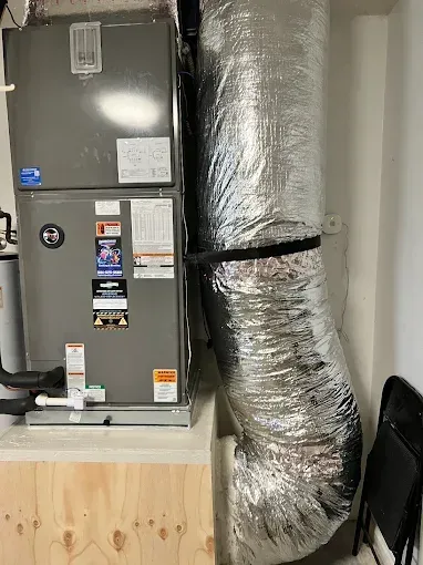 Gray HVAC unit with silver insulated ducting in a utility room