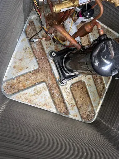 Close-up of a dirty HVAC unit with copper pipes and a black compressor inside a metal cabinet